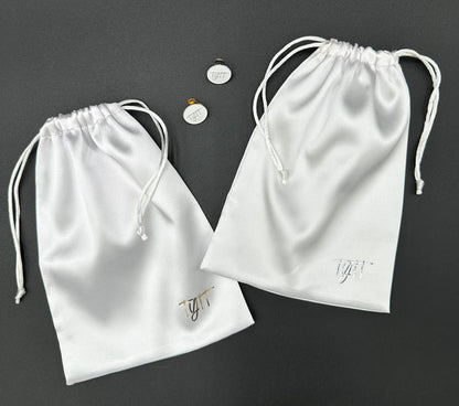 a pair of white satin drawstring bags next to a coin